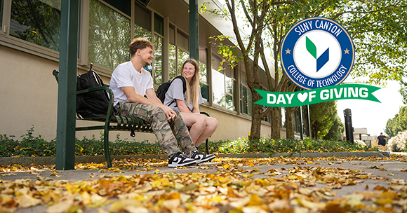 Day of Giving - Two students sit on a bench in the academic plaza on a fall day.