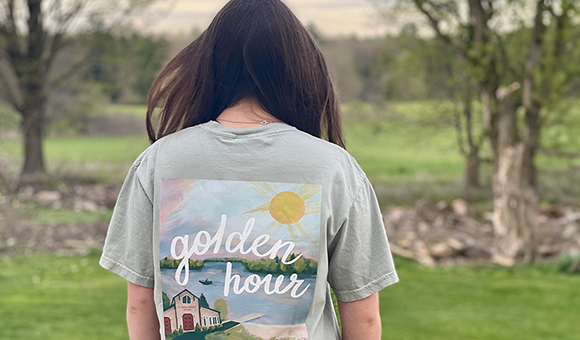 High School student Rileigh Stebbins models a Golden Hour t-shirt while standing in a forest.