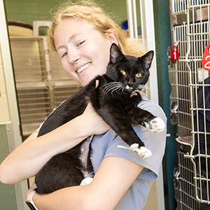 A Veterinary Technology student holds a black cat with white paws.