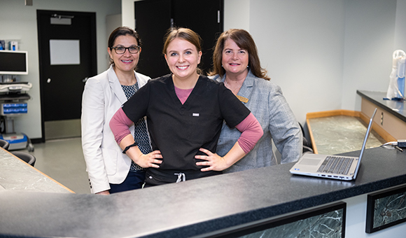 Faculty members Marela Fiacco and Vicki Perrine stand in a trio with a student.