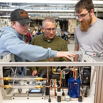 Instructor Jay Simmons works with two students on a heat pump.