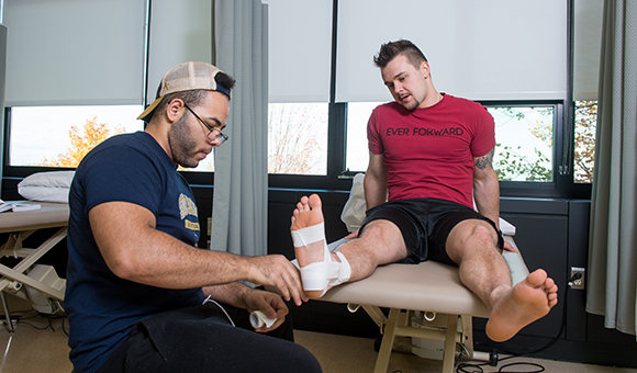 A student tapes an athlete's ankle.