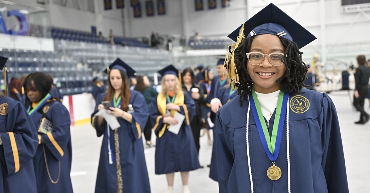 A graduate poses in the Ice Arena prior to Commencement.