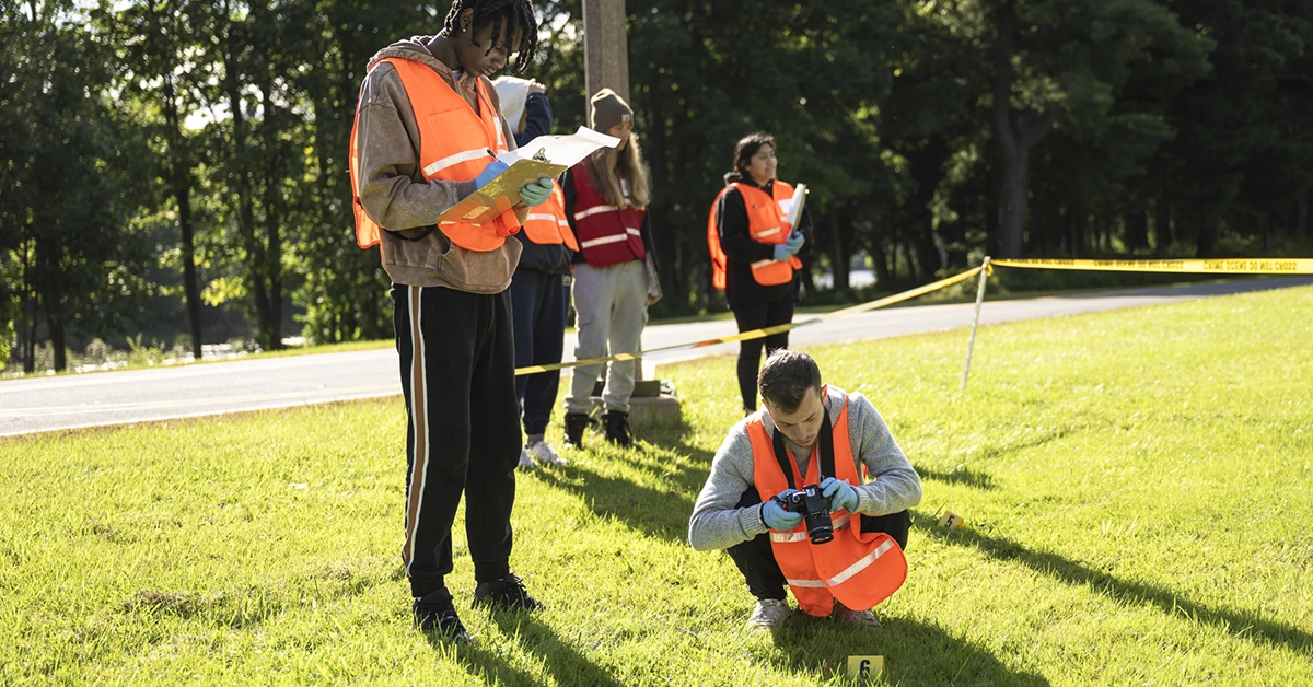 A student takes notes while another photographs evidence at a mock crime scene.