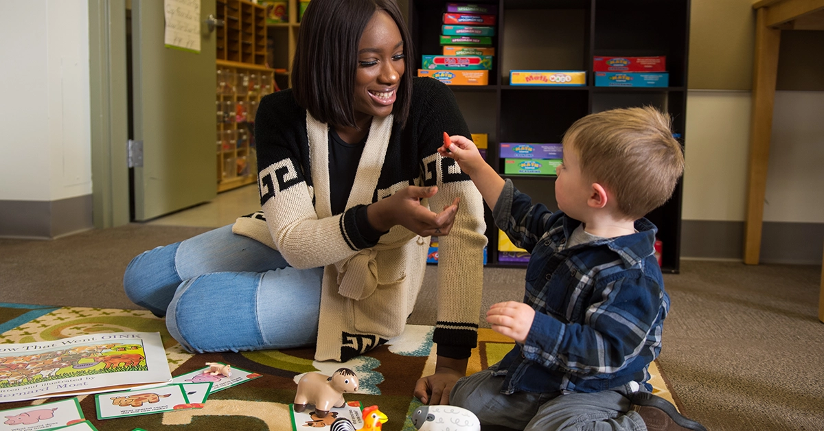 A toddler hands a student a toy carrot in the Early Childhood Education Center.
