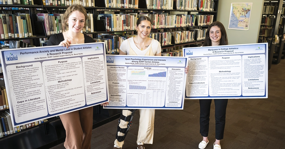 Three Applied Psychology students hold up their research posters at the Scholarly Activities celebration.