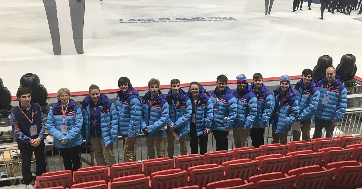 Sports Management students wearing blue FISU jackets line up in Herb Brooks Arena in Lake Placid.