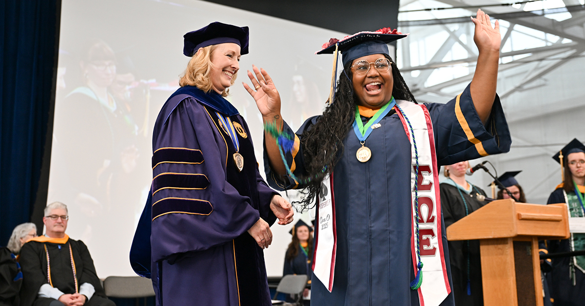 A graduate waves to the crowd while passing Dean Michele Snyder on stage.