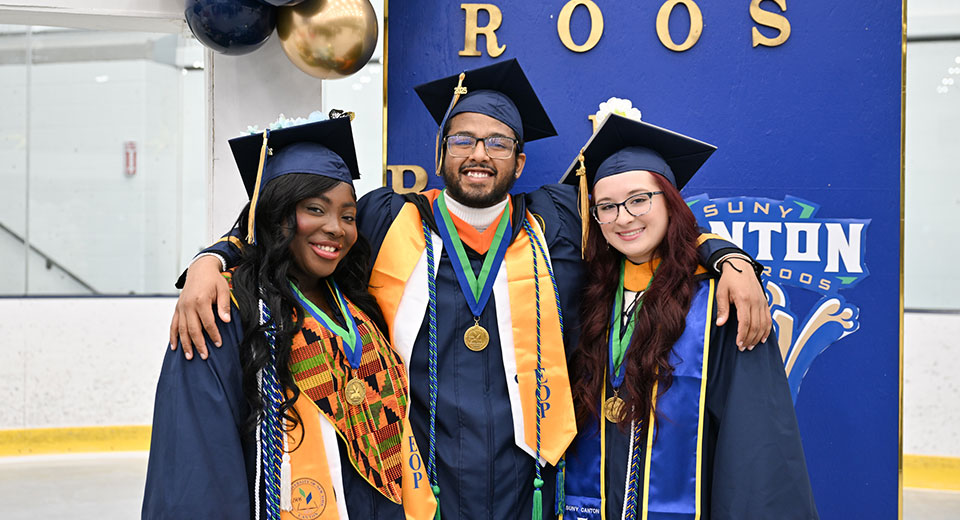 Three decorated graduates pose for a photo in the ice arena prior to Commencement.