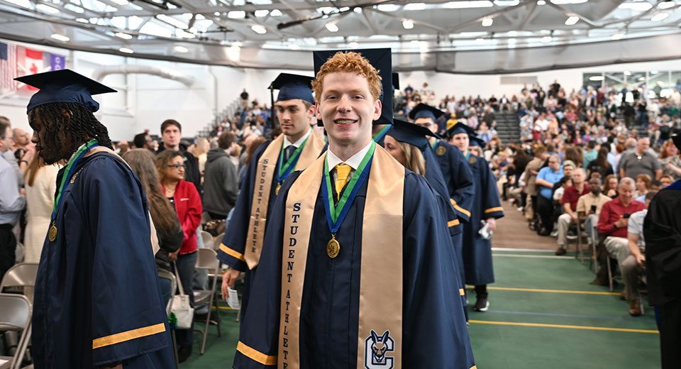 A graduate poses while in the Commencement 2025 processional lineup.