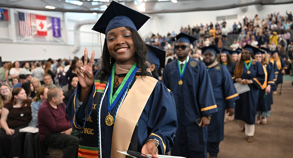 A graduate poses while in the Commencement 2025 processional lineup.