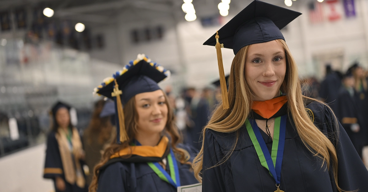 Two students smile in their regalia prior to Commencement 2026.