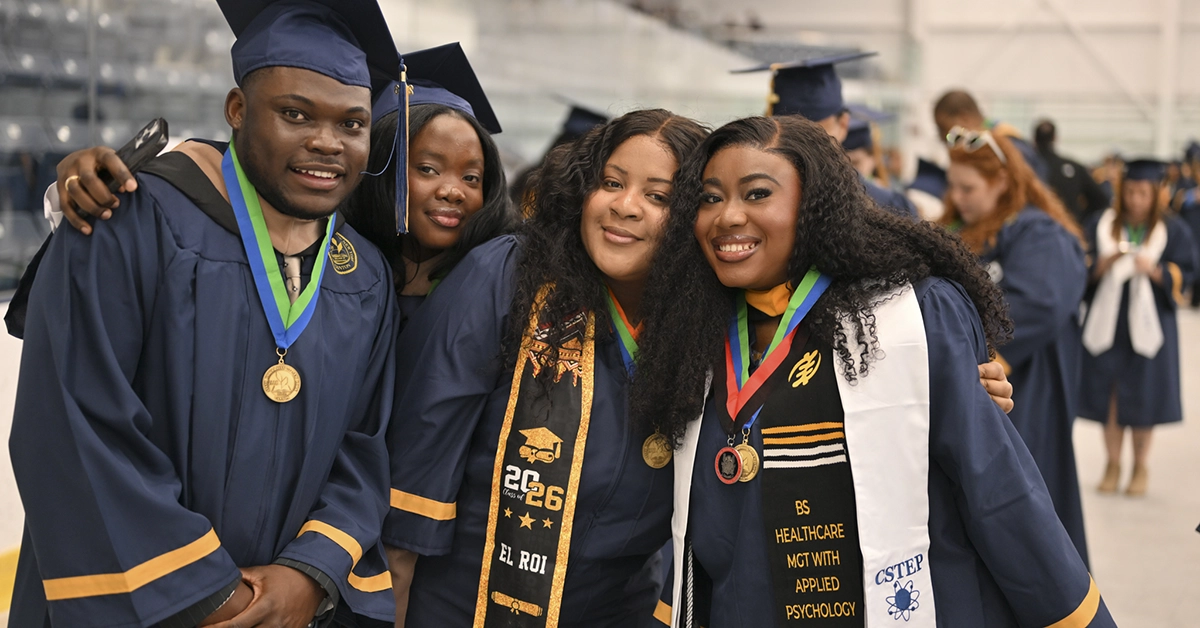 Four graduates pose for a photo in ice arena prior to Commencement 2026.