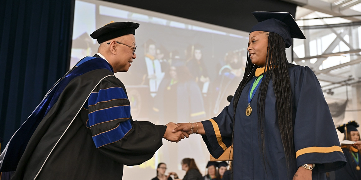 A graduate shakes hands with Dean Kenneth Rhee on the Commencement stage.