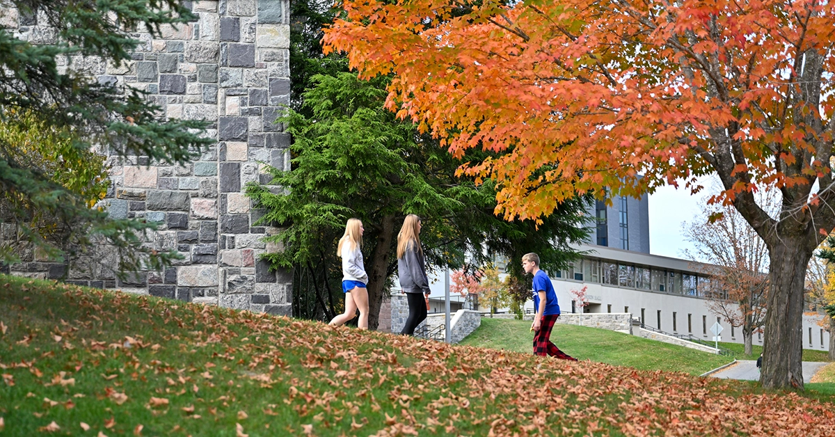Bright orange fall foliage takes center stage as students walk along a path near Miller Campus Center.