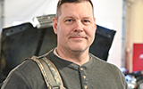 Eric Armstrong holds a camouflaged back pack in the Automotive Technology lab.