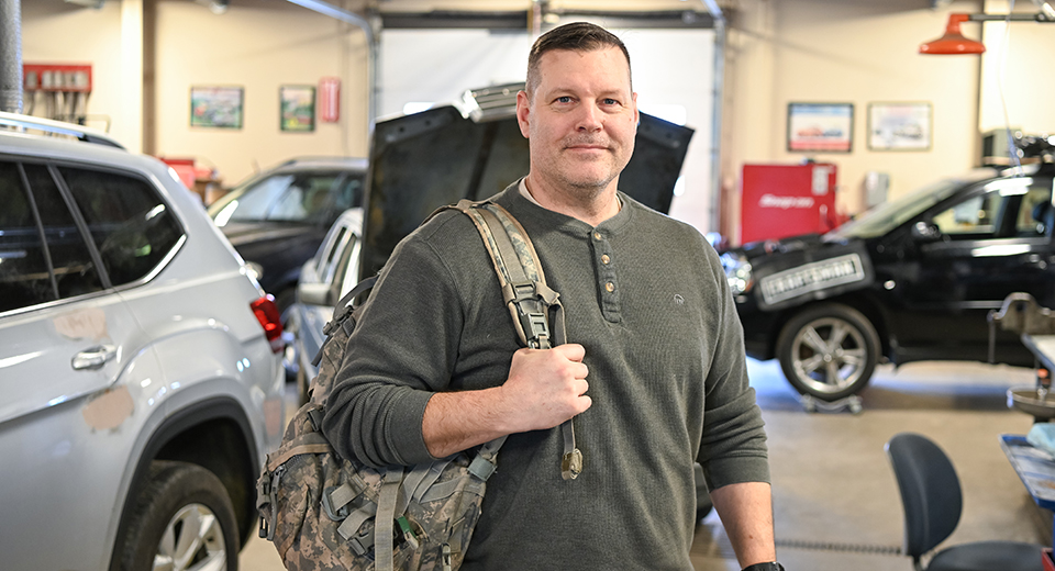 Eric Armstrong holds a camouflaged back pack in the Automotive Technology lab.