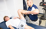 Physical Therapist Assistant student Connor Dickinson stretches an athlete's leg on a table.