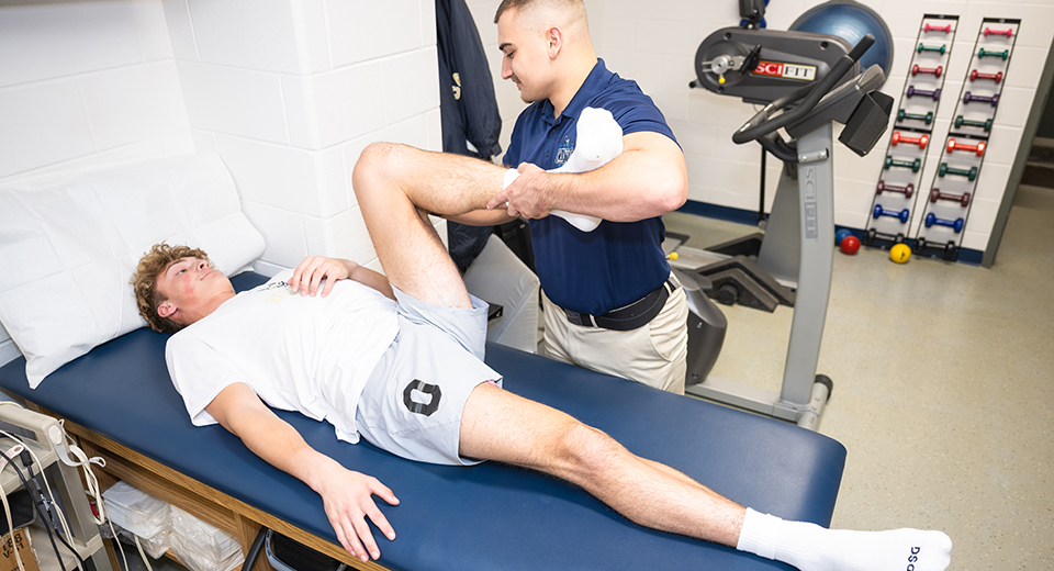 Physical Therapist Assistant student Connor Dickinson stretches an athlete's leg on a table.
