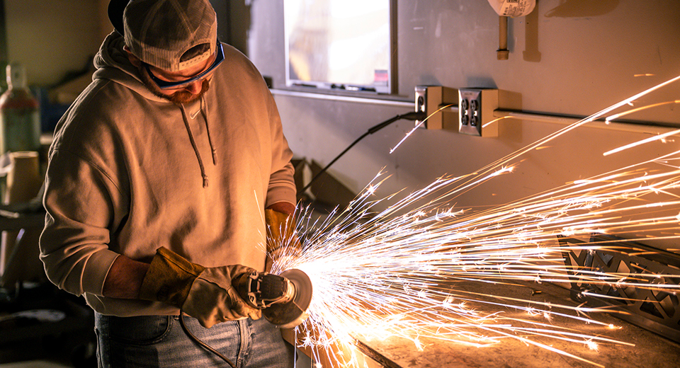 Samuel Servati grinds a part while sparks fly around in the Mechanical Engineering Tech lab.