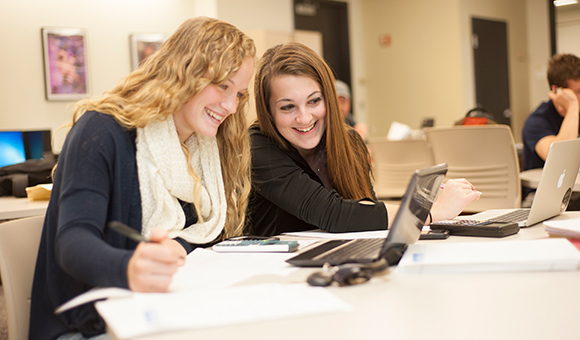 Two students study on their laptops in the library