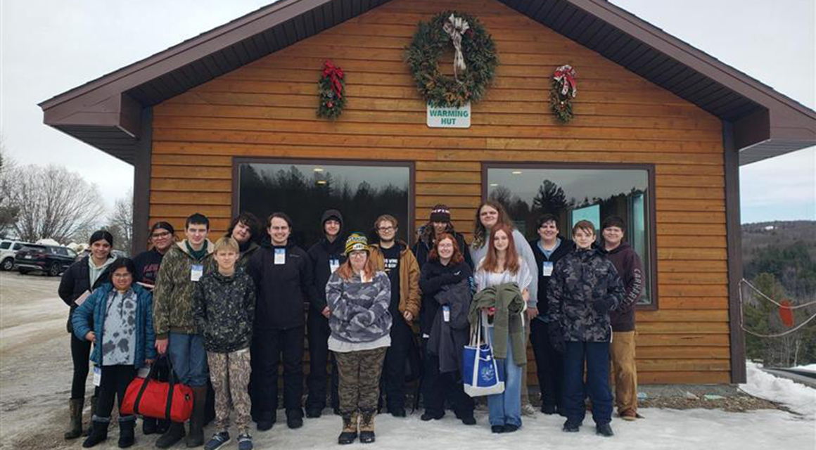 Liberty students outside the log cabin entrance to Titus Mountain.