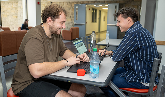 Two students work on laptops across from each other near Roos Court in MacArthur Hall.