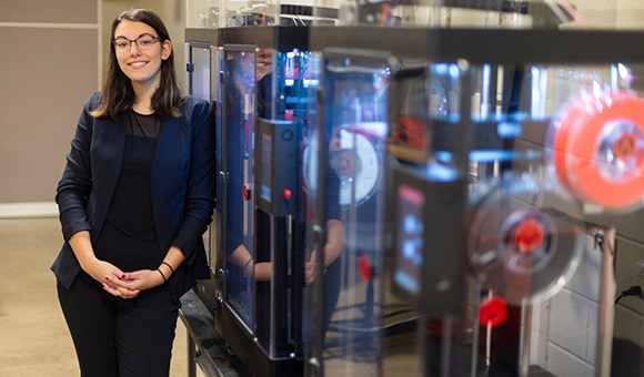 Maelea Mercado stands in front of a row of 3D printers in the Mechatronics Lab
