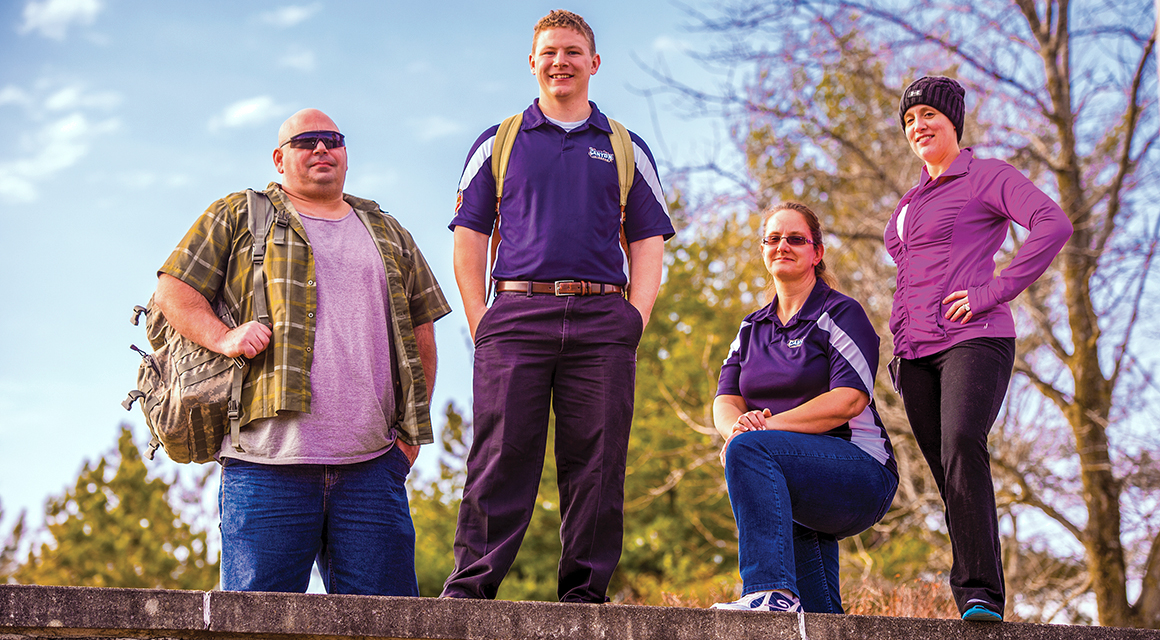 Four veteran students stand along the top of a campus wall.