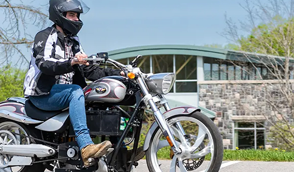 A student rides a motorcycle past Newell Vet Tech Center.