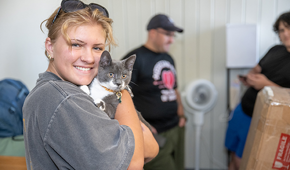 A student holds a gray and white striped cat during move-in day.
