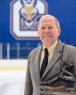 Bill Mein stands in front of the SUNY Canton Ice Arena with figure skates over his shoulder.