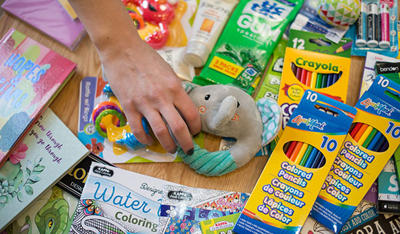 A hand grabs an elephant rattle from among the children's toys and art supplies.