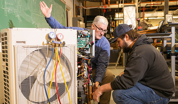 Dean Michael Newtown demos a heat pump in class while a student looks on.