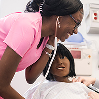 A nursing student checks the vitals of a dummy in class.