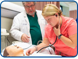 A student uses a stethoscope on a manikin while a faculty member looks on.