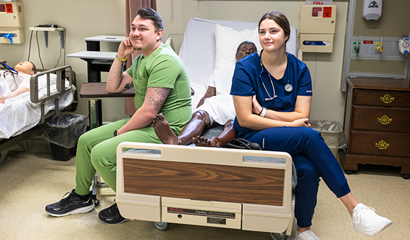 Two nursing students sit and pose in the Nursing Lab.