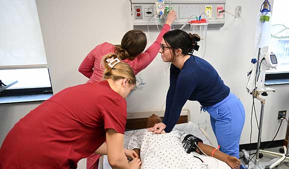 Three students participate in a training exercise in the Nursing Simulation Lab.