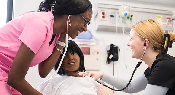 Nursing students check the vitals of a test manikin in the Nursing lab.