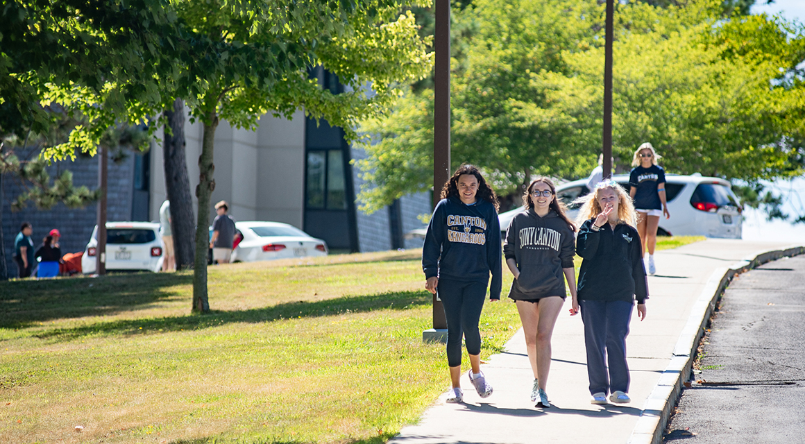 Three students walk down a sidewalk on a sunny move-in day at SUNY Canton.