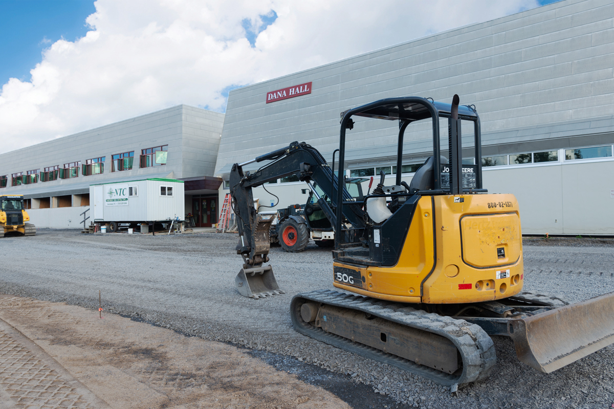 An excavator levels gravel in front of Dana Hall.