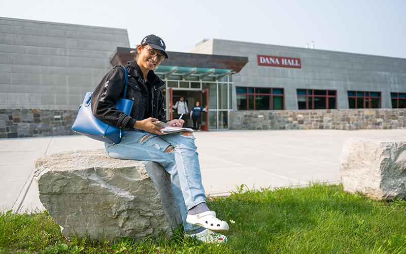 A student sits on a rock outside of the new Dana Hall.