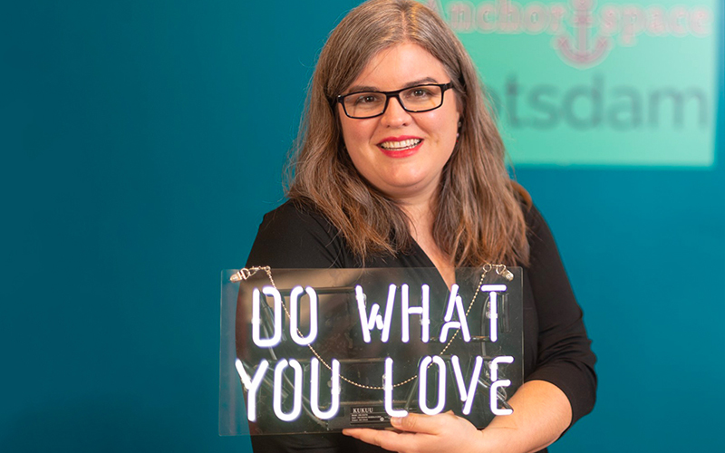 Nicole Ouellette of Breaking Even Communications holds up a Do What You Love sign.
