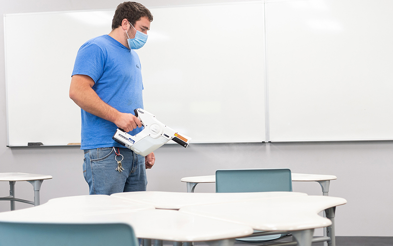 A custodian sprays disinfectant in a classroom.