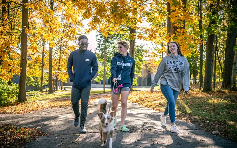 Students walking around campus with a dog on a beautiful fall day.