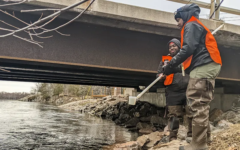 Two students take water samples under a local bridge.