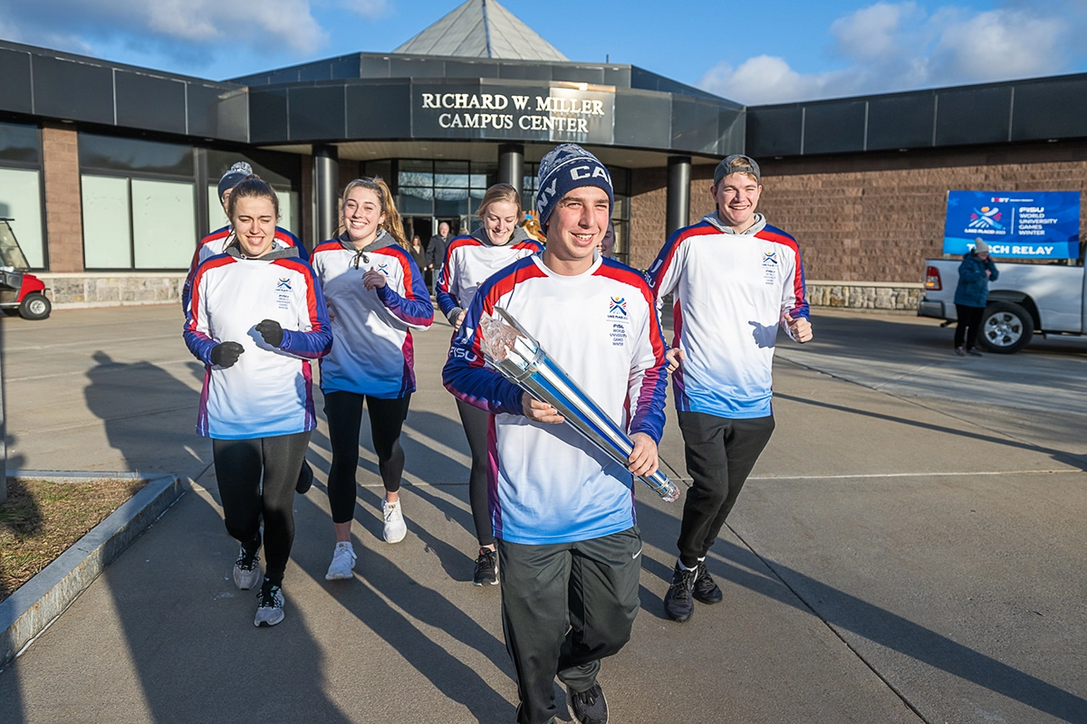 SUNY Canton student athletes carry the FISU torch outside the Miller Campus Center.