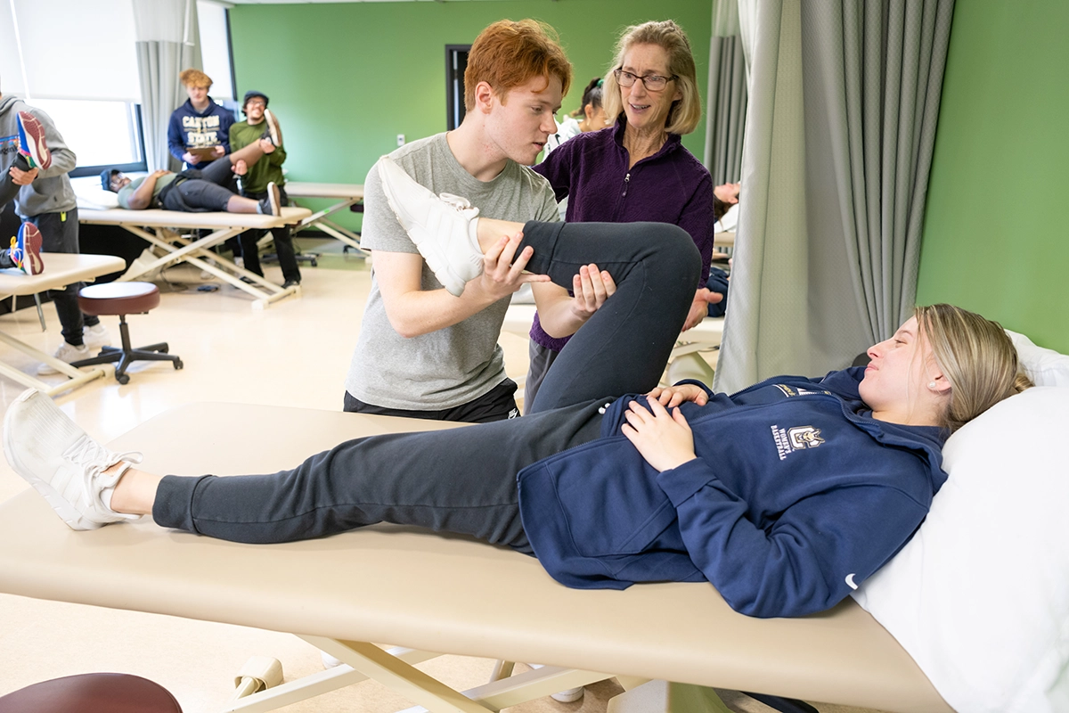 A student assists another student with leg stretches while an instructor looks on in the Physical Therapist Assistant lab.
