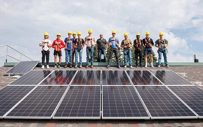 A group of students stands on peak of a mock solar roof.