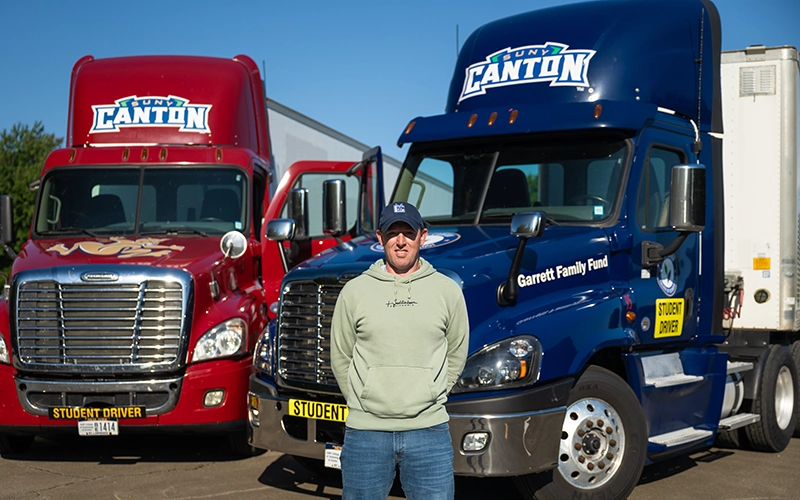 Ryan Hartigan stands in front of SUNY Canton's CDL fleet, featuring donations by the Garrett Family.